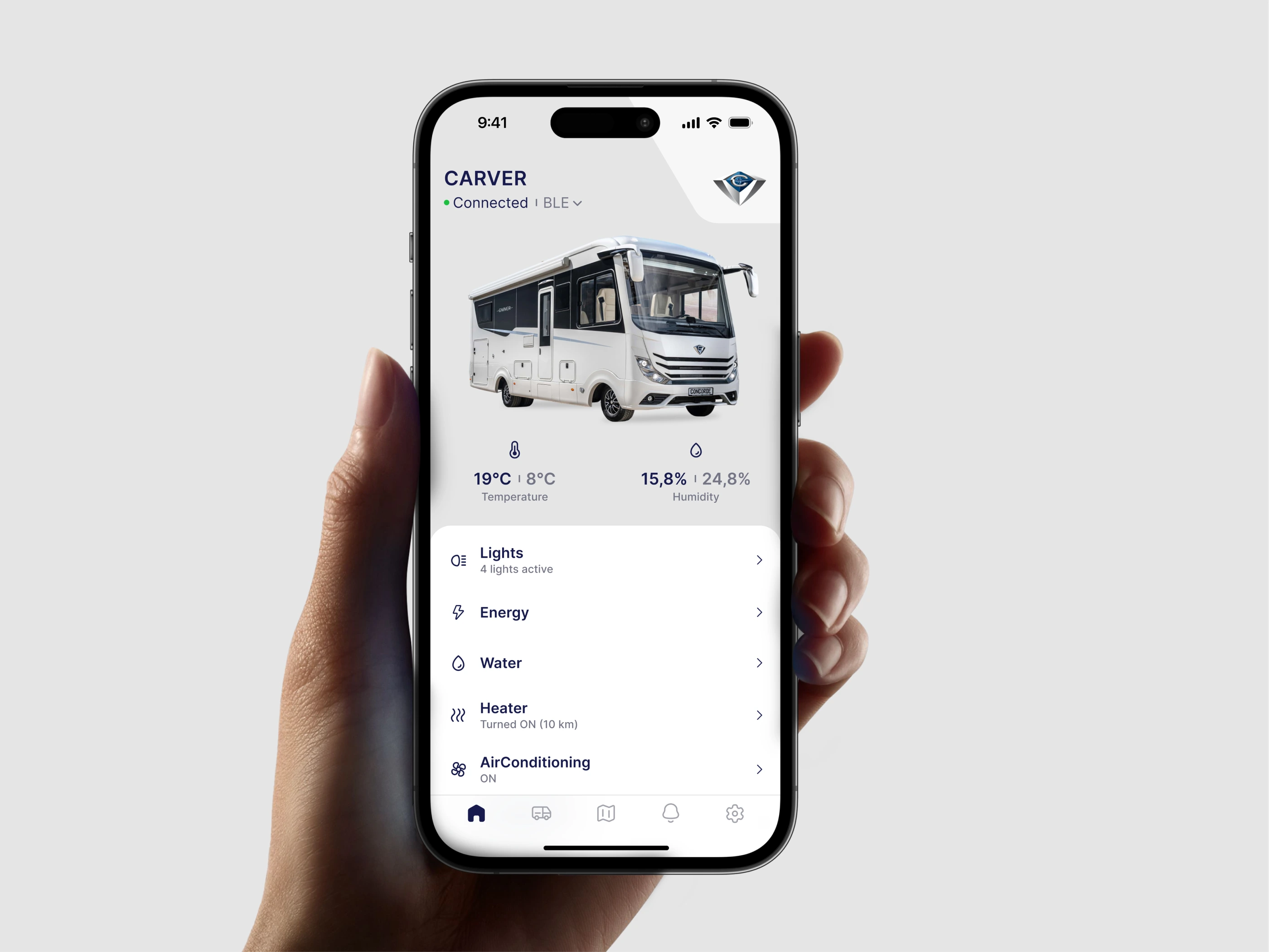 The Concorde app's Carver dashboard held in one hand, showing the motorhome, its temperature and humidity, and the lights, energy, water and heater controls