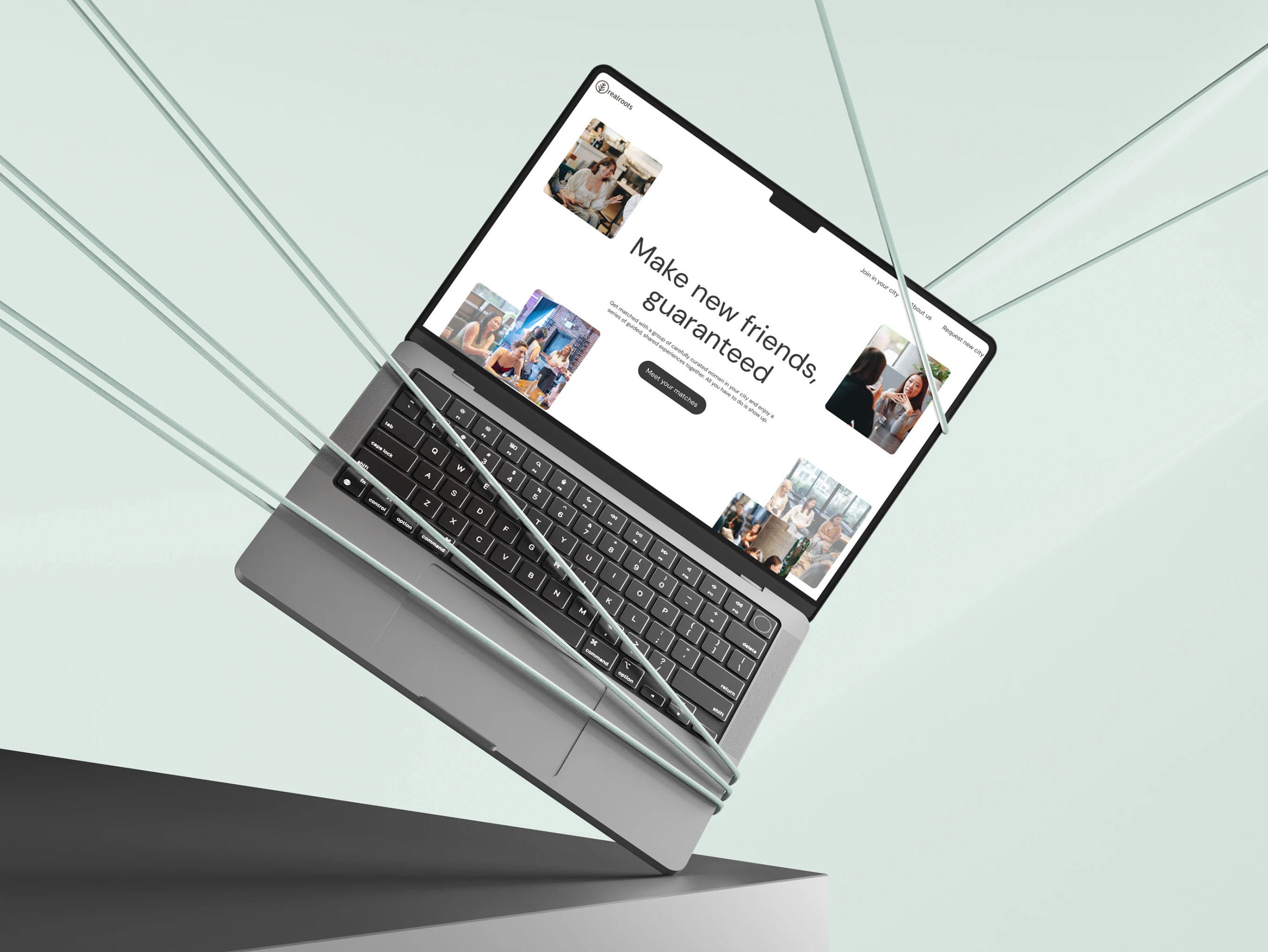 The RealRoots marketing website on a laptop held at an angle in pale green cords, its home page headlined Make new friends, guaranteed